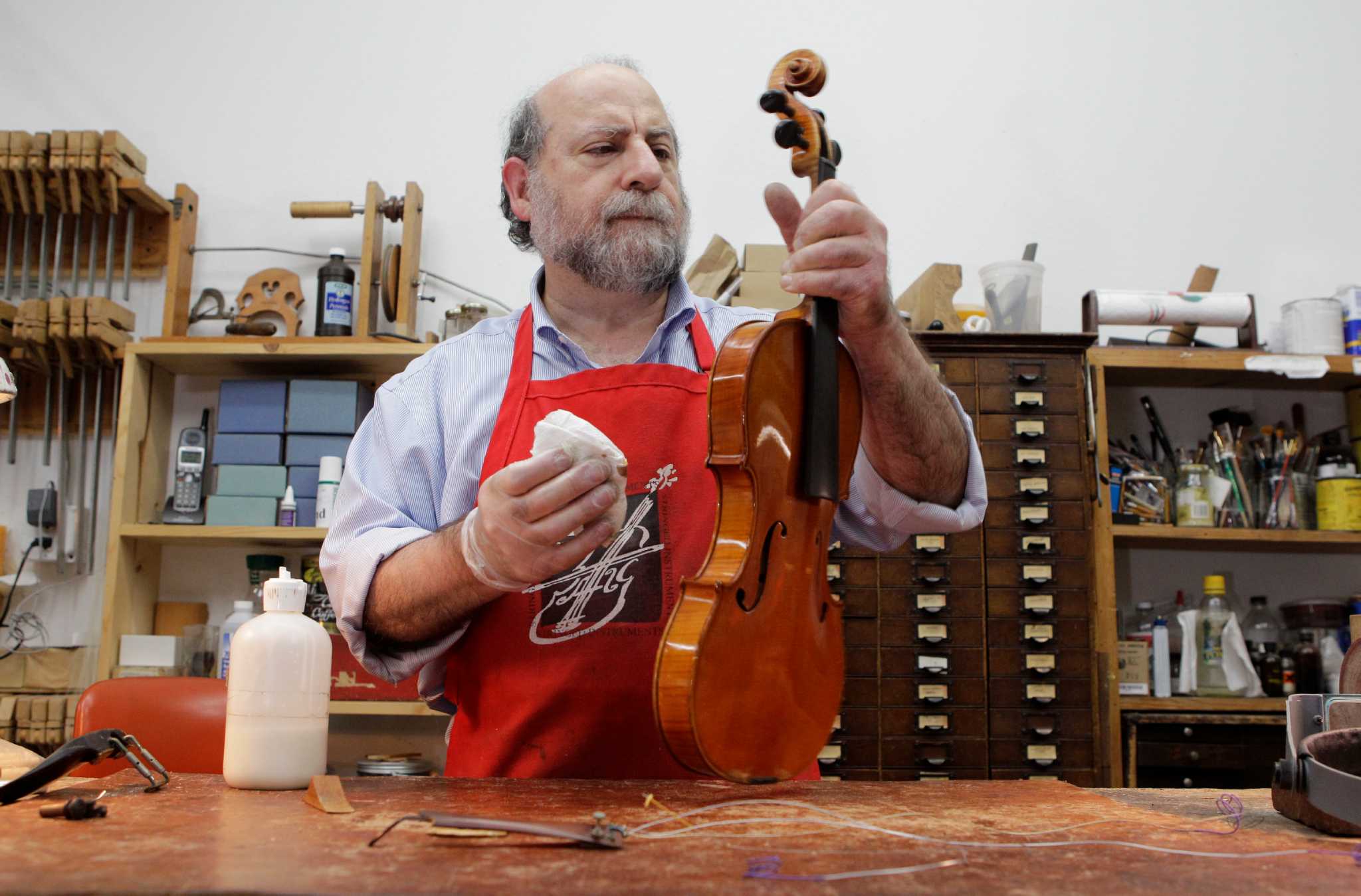 Philip Gold at his workbench in the Gold Violin Shop, holding a violin by the neck